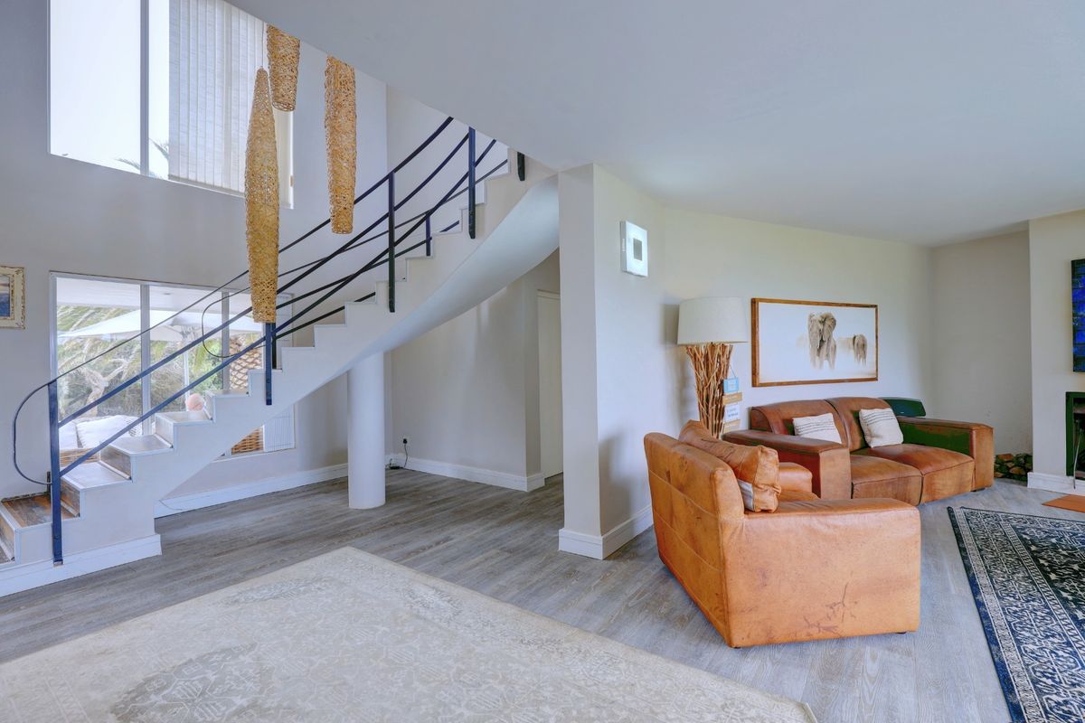 Spacious living area featuring a striking staircase with metal balustrade, double volume ceilings, and modern laminate flooring, creating an open and airy atmosphere.