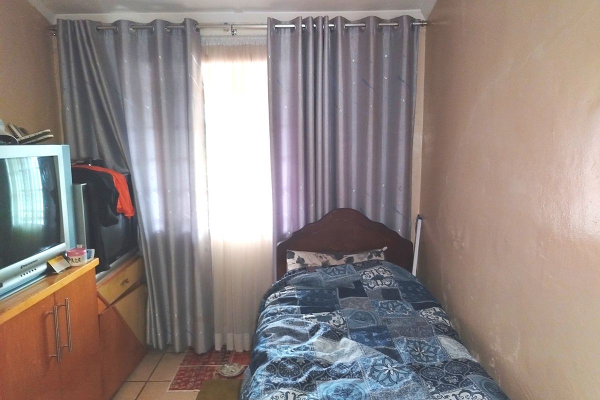 A compact bedroom featuring tiled flooring and a window with curtain treatments. The room requires cosmetic updates to the wall finishes.