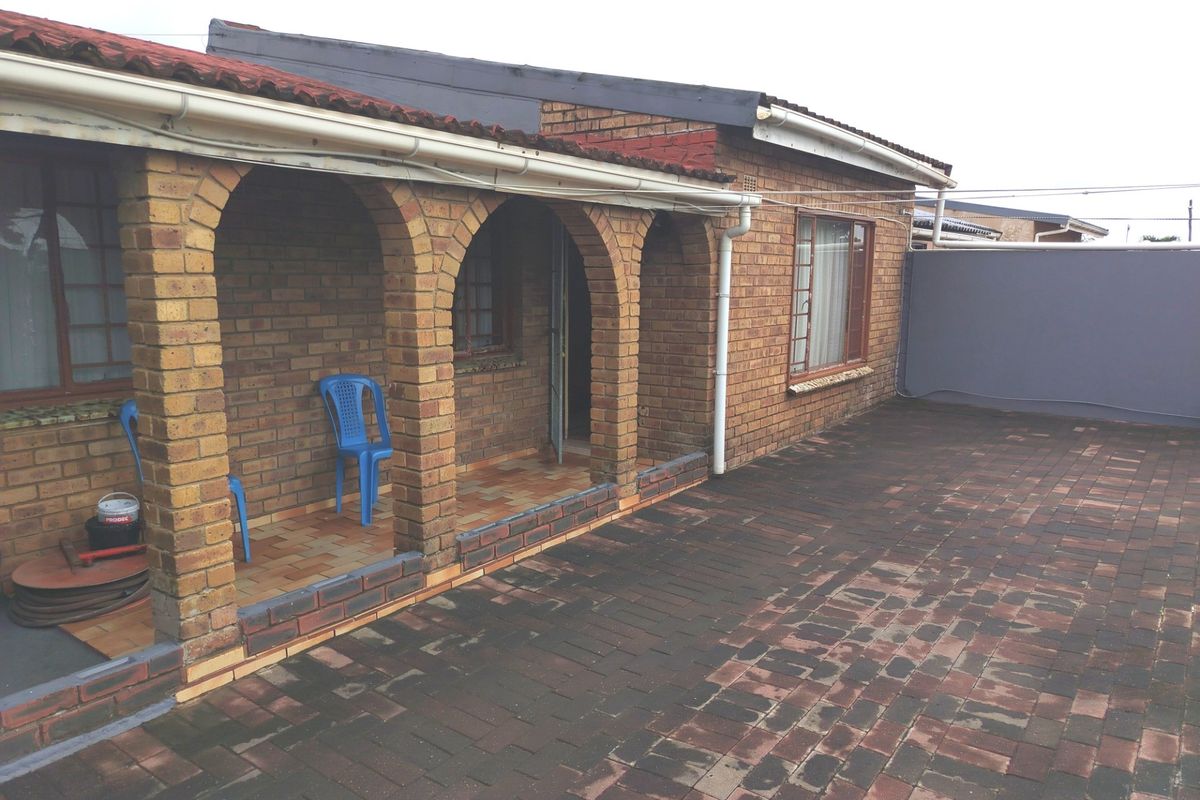 A rear exterior view featuring a brick facade with an arched veranda and a paved courtyard area.
