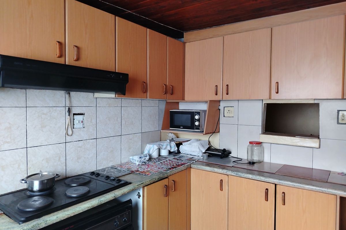 A dated kitchen featuring laminate cabinetry, built-in oven, electric hob, and tiled splashbacks, offering significant potential for a modern renovation.