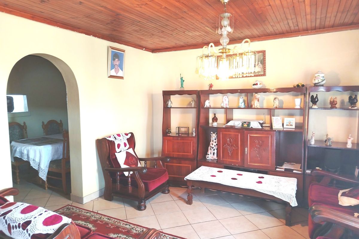 A living room featuring a timber tongue and groove ceiling, ceramic floor tiles, and an arched doorway leading to an adjacent dining area.