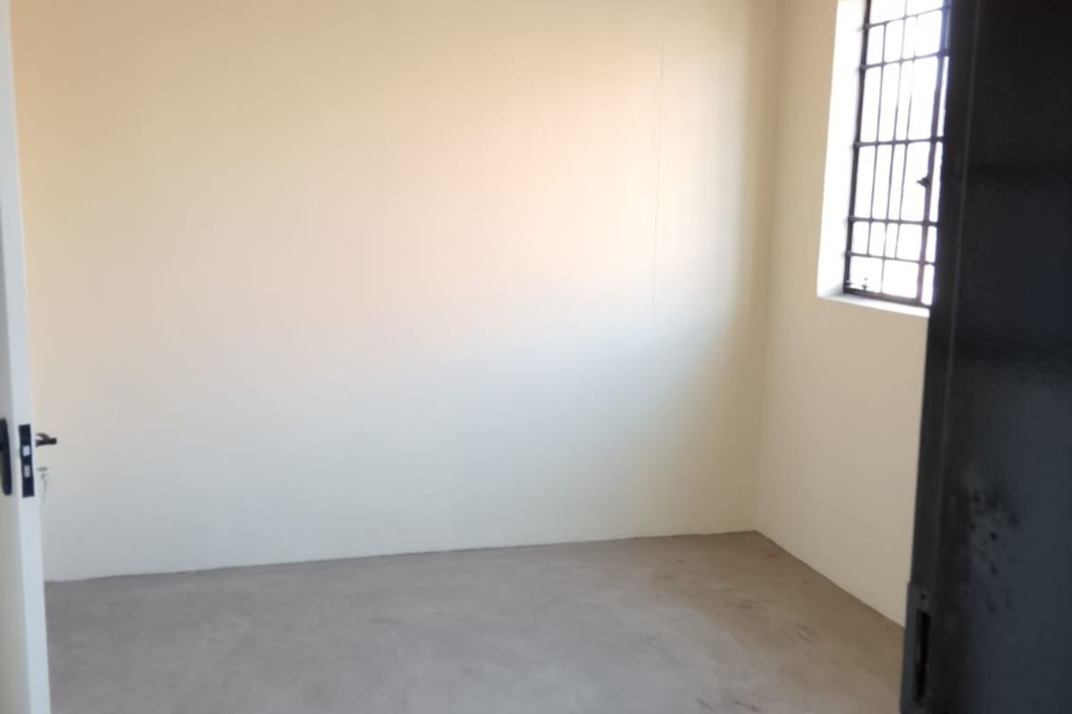A clean, empty room featuring polished concrete flooring, track lighting, and a window fitted with security bars.