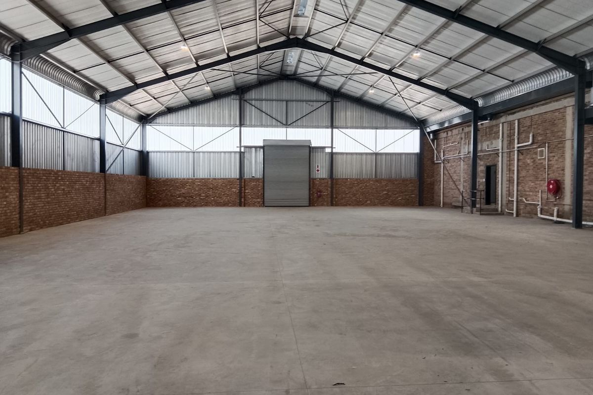 Spacious industrial warehouse featuring a high-clearance steel portal frame, polished concrete flooring, exposed brick walls, and a large roller shutter door for easy access.