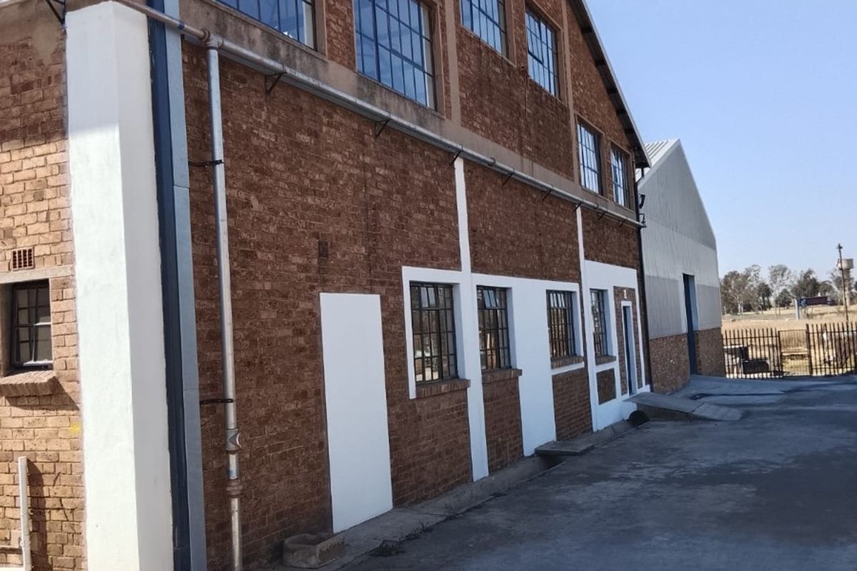 Side view of an industrial building featuring exposed brickwork, large steel-framed windows, and a concrete driveway.