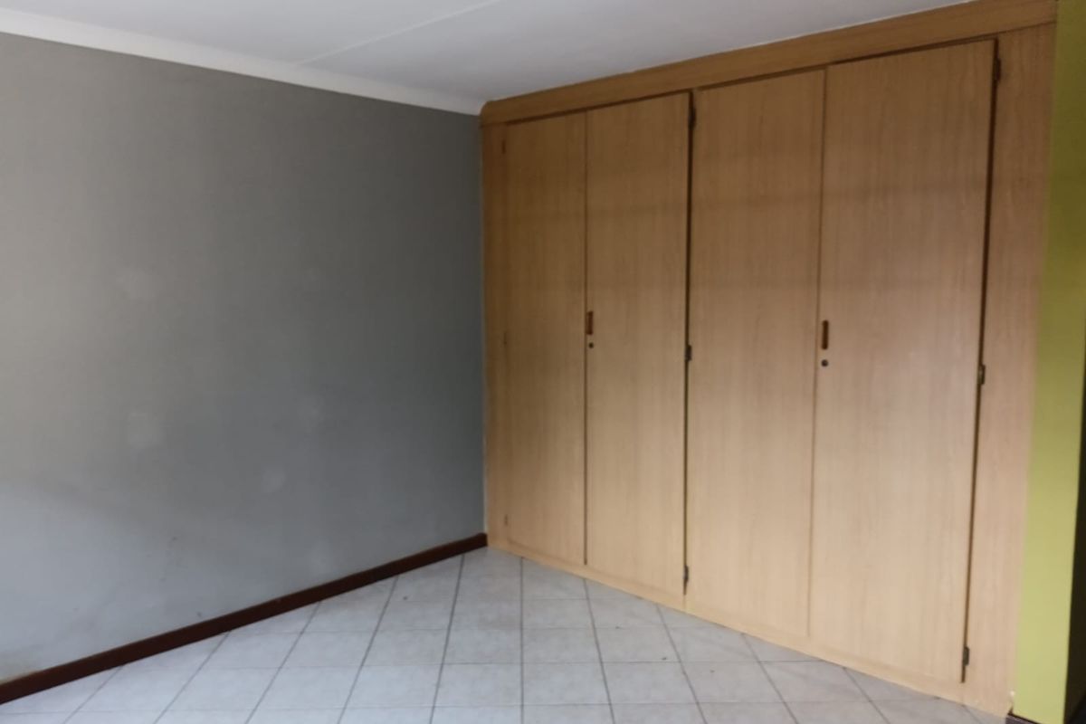A vacant bedroom featuring neutral tiled flooring and extensive built-in wooden cupboards, offering a blank canvas for personalization.