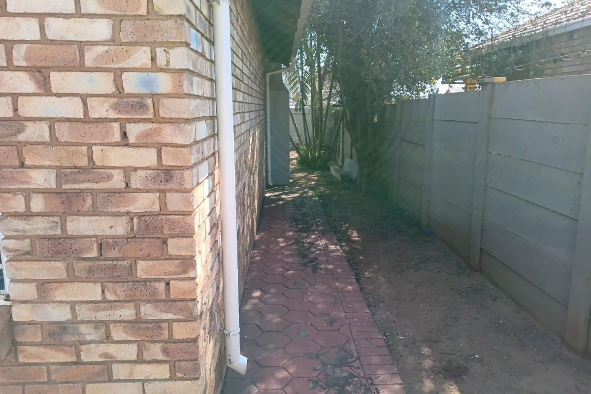 A narrow side passage featuring face brick exterior walls, a paved walkway, and a precast concrete boundary wall.
