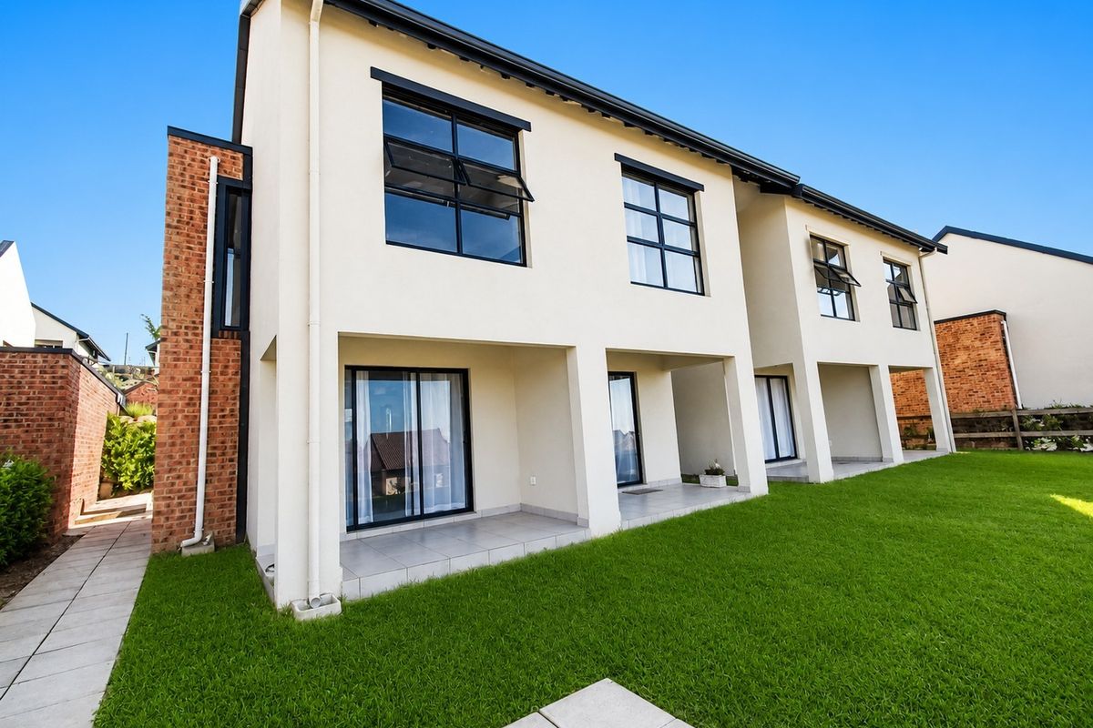 Rear view of a modern apartment building featuring a covered tiled patio, large sliding glass doors, and well-maintained lawn area.