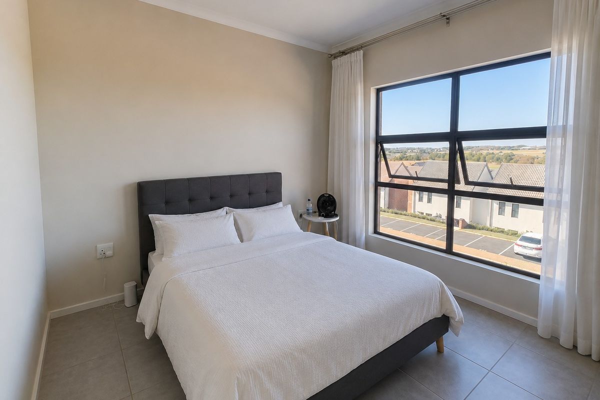 A bright and modern bedroom featuring large aluminium-framed windows with natural light and neutral tiled flooring.