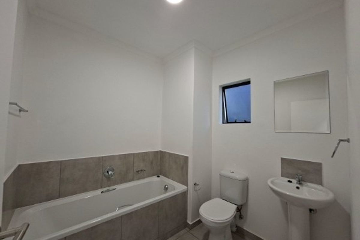 A clean, modern bathroom featuring a bathtub with tiled surround, a pedestal basin, and a toilet, finished with neutral wall tones.