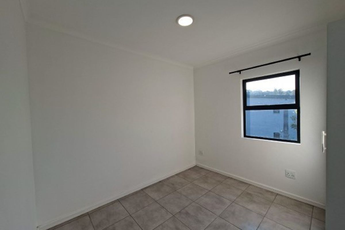 A clean, empty bedroom featuring neutral tiled flooring, white walls, and a single window with a curtain rod.