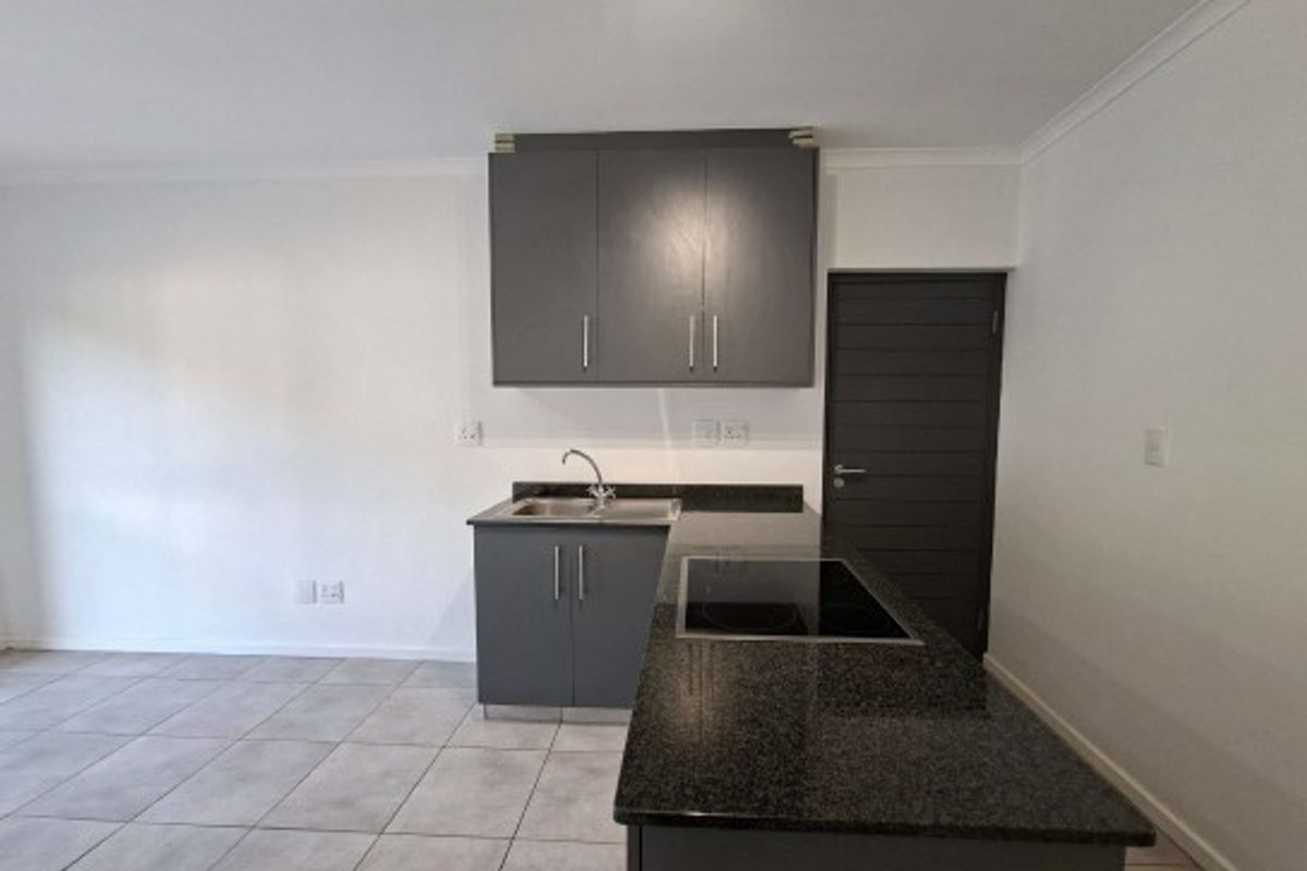 Modern kitchen featuring dark grey cabinetry, granite countertops, integrated electric hob, and tiled flooring in a clean, minimalist layout.