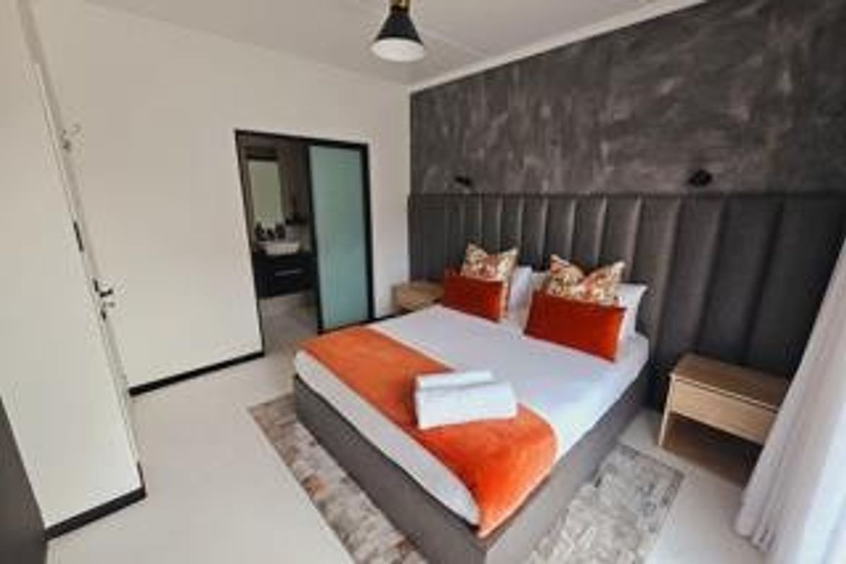 A modern bedroom featuring a large upholstered headboard, built-in storage, and direct access to an en-suite bathroom with contemporary finishes.
