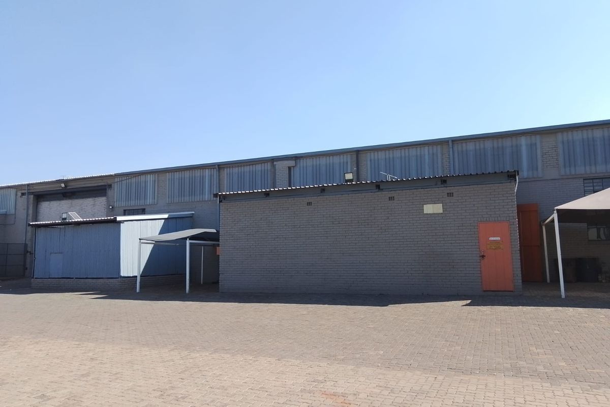 Rear exterior view of an industrial warehouse facility featuring brick construction, corrugated metal roofing, and a paved yard area.