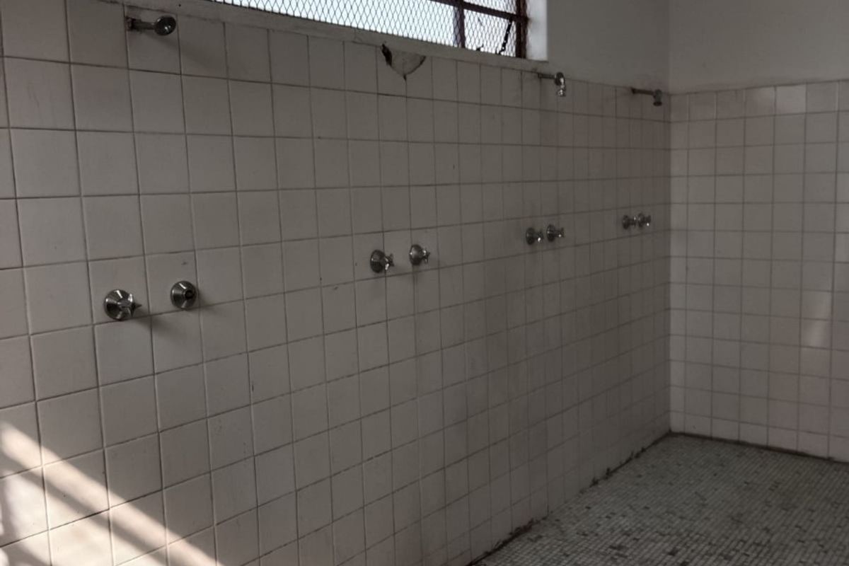 Industrial communal shower facility featuring multiple wall-mounted shower heads, tiled surfaces, and a high-level security mesh window.