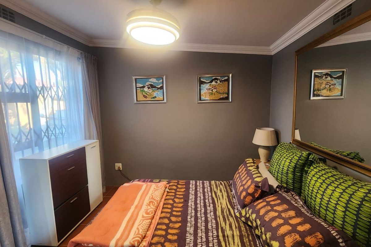A cozy bedroom featuring a ceiling fan, decorative cornice, and a large wall-mounted mirror, with a security gate installed on the window.