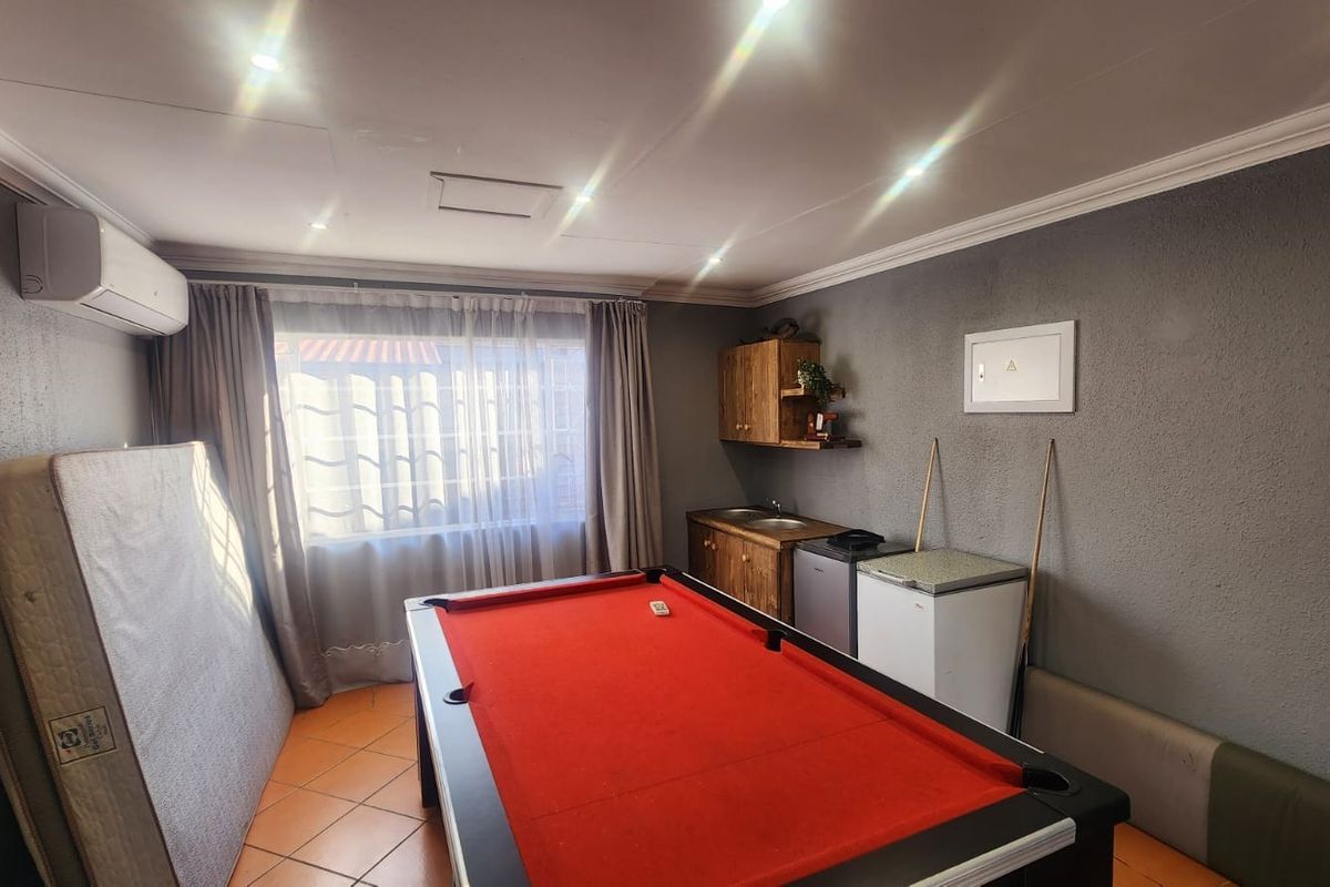 A multi-purpose living area featuring tiled flooring, recessed lighting, a split-system air conditioner, and a built-in kitchenette unit with a sink.