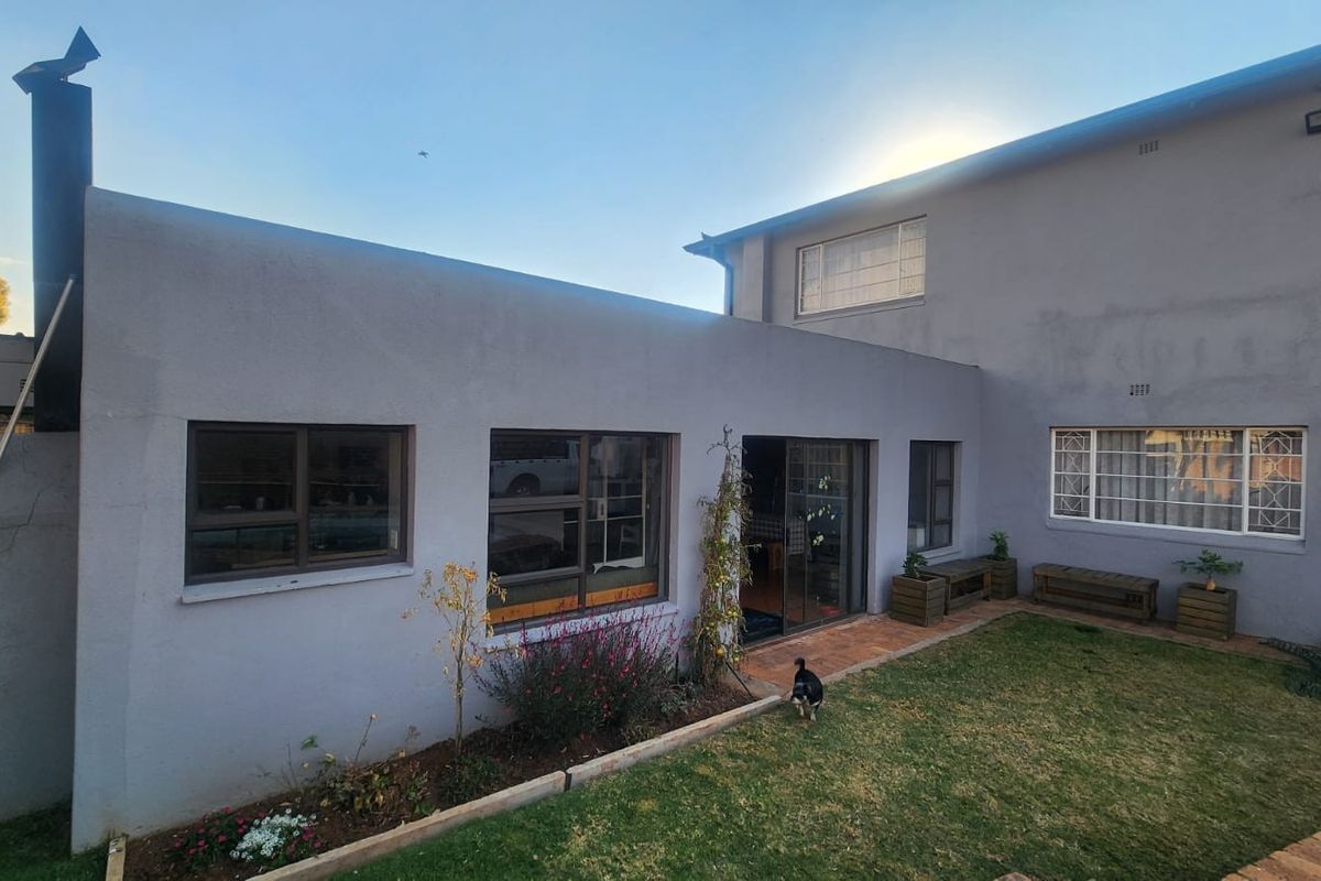 Rear view of the property featuring a paved patio area, sliding glass doors, and an external chimney stack against a rendered wall finish.
