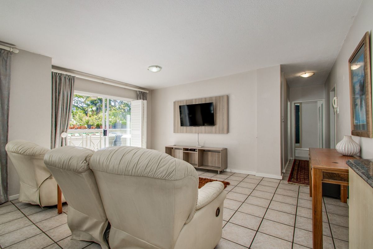 A bright living room featuring tiled flooring, a wall-mounted TV unit, and a sliding glass door providing access to an outdoor patio area.