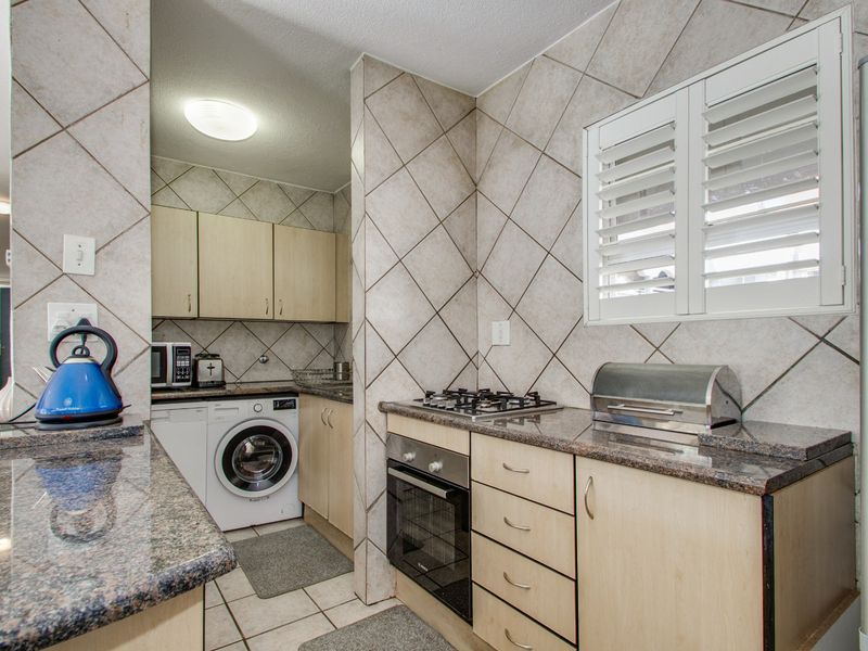 Compact kitchen featuring granite countertops, built-in oven, gas hob, and integrated cabinetry with a tiled backsplash and shutter window.