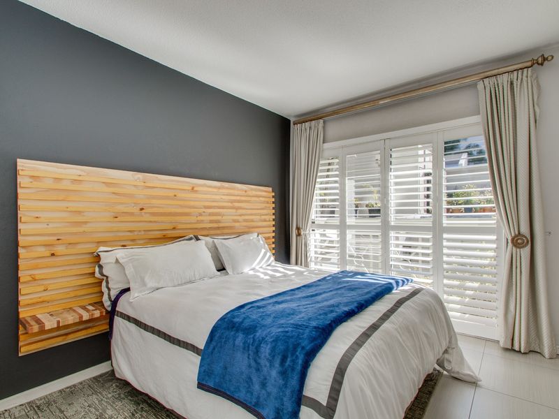 A well-maintained bedroom featuring a dark accent wall, tiled flooring, and white plantation shutters providing natural light.