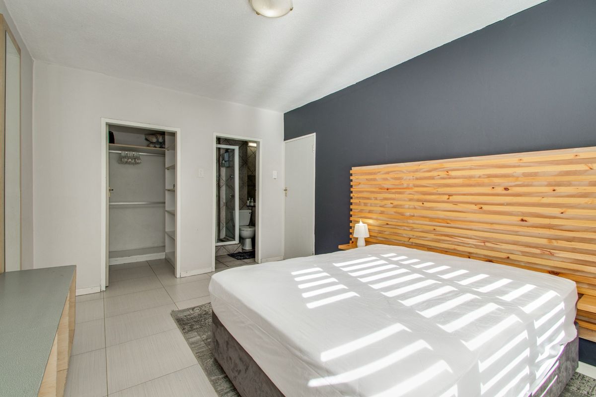 A well-maintained bedroom featuring tiled flooring, a dark accent wall, a built-in closet, and direct access to an en-suite bathroom.