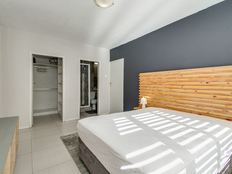 A well-maintained bedroom featuring tiled flooring, a dark accent wall, a built-in closet, and direct access to an en-suite bathroom.