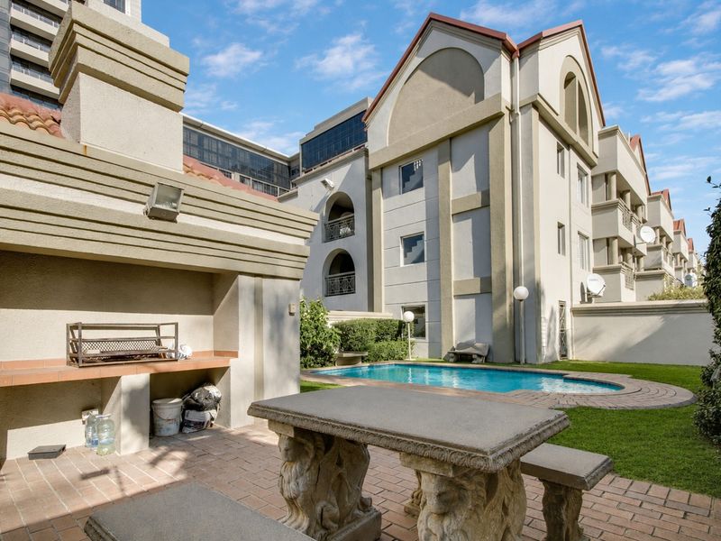 Communal outdoor entertainment area featuring a swimming pool, paved patio, and a built-in braai facility within the apartment complex.