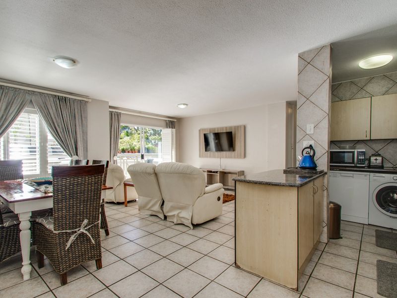 Open-plan living and dining area featuring tiled floors, a functional kitchen with granite countertops, and direct access to a balcony through sliding doors.