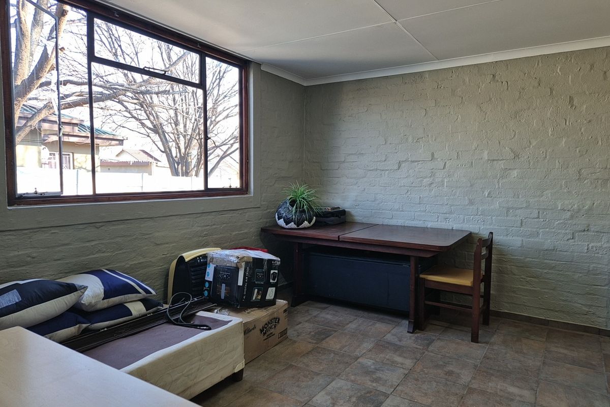 A living area featuring painted brick walls, large windows providing natural light, and tiled flooring, offering a blank canvas for renovation.