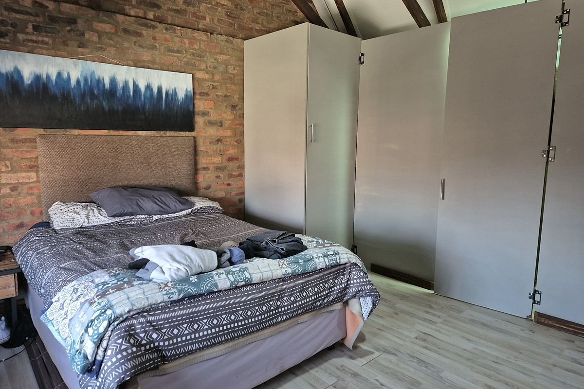 Bedroom featuring exposed brick walls, vaulted ceiling with timber rafters, laminate flooring, and integrated built-in cupboards.