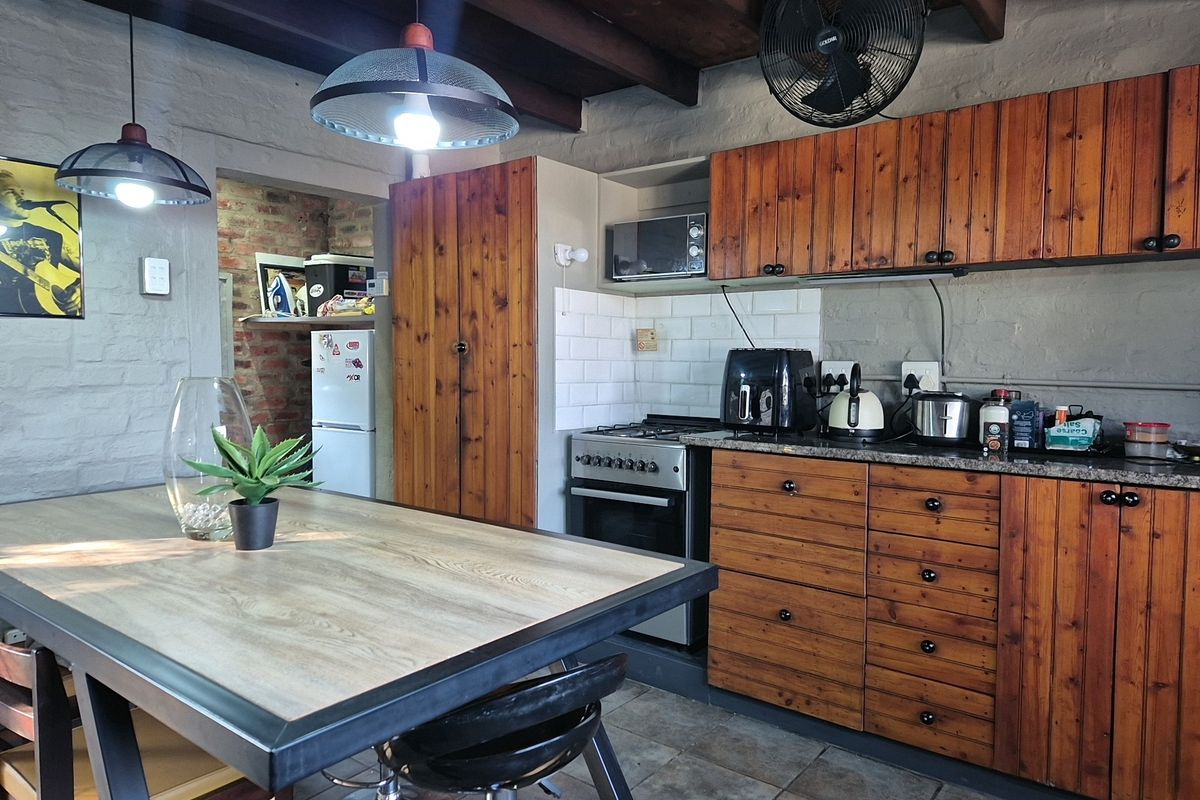 Rustic kitchen featuring wooden cabinetry, granite countertops, gas stove, subway tile backsplash, and exposed timber ceiling beams.