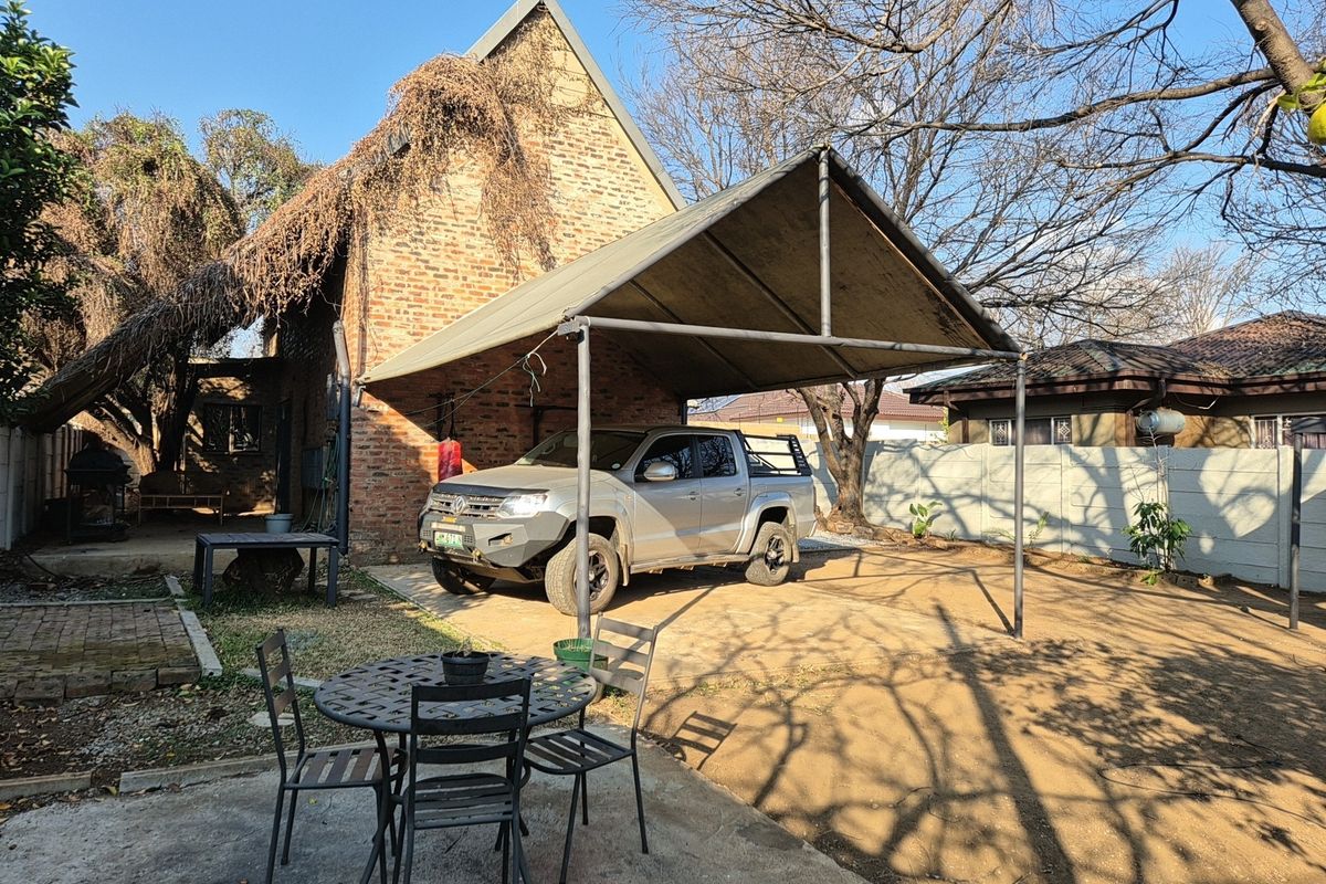 Rear exterior view featuring an exposed brick facade, a metal carport structure, and a large unpaved yard area with boundary walling.