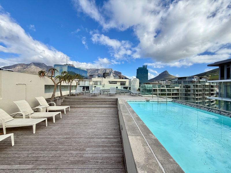 Rooftop swimming pool area featuring timber decking and panoramic city and mountain views.