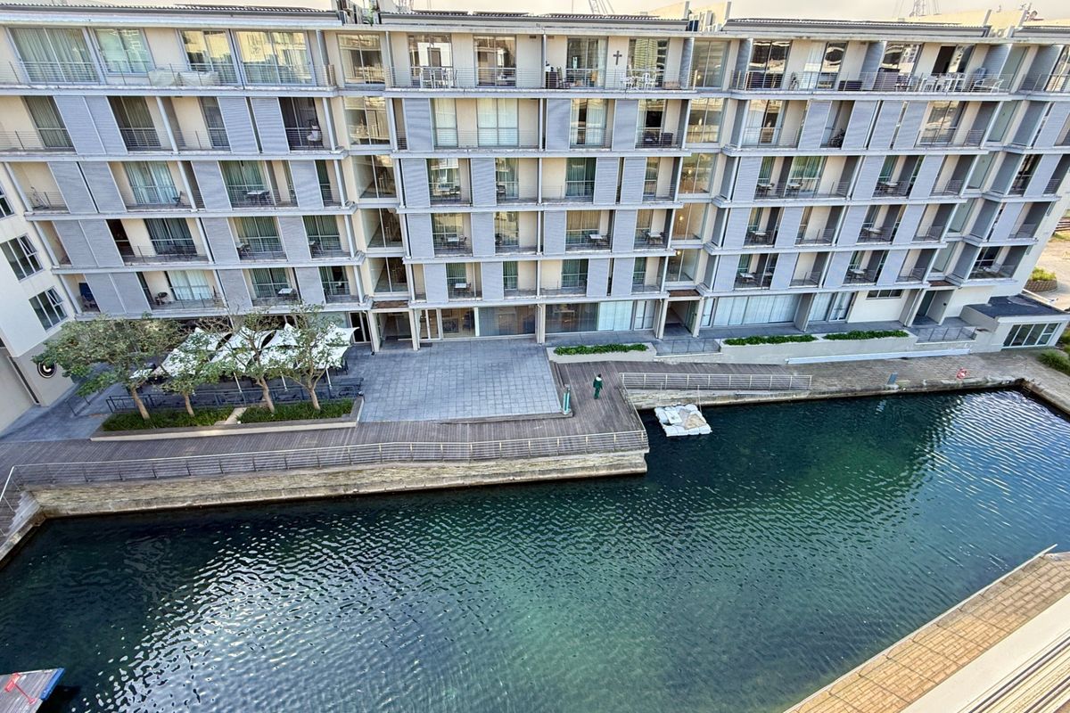 Elevated view of a modern apartment complex facade featuring private balconies, timber decking, and direct canal frontage.