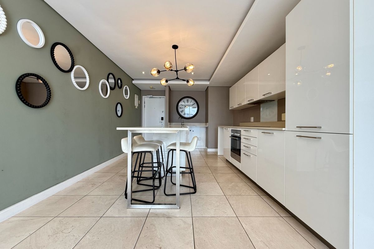 Modern kitchen featuring sleek white cabinetry, built-in oven, stone floor tiles, and a central breakfast bar, creating a clean and functional culinary space.
