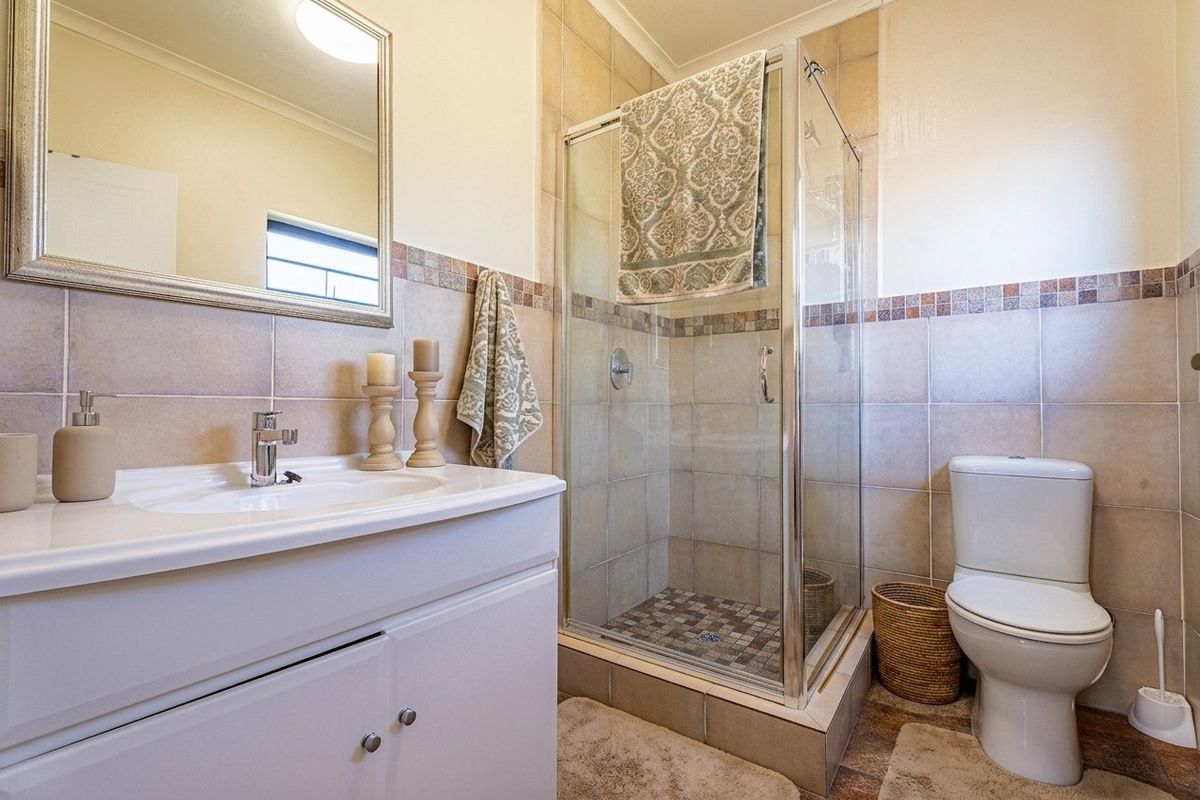 A functional bathroom featuring a vanity cabinet with basin, a glass-enclosed shower, and neutral ceramic wall tiling.