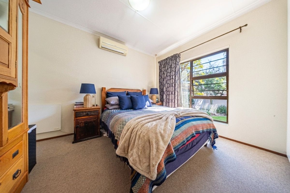 A well-lit bedroom featuring carpet flooring, a wall-mounted split-system air conditioner, and a large window with natural light.