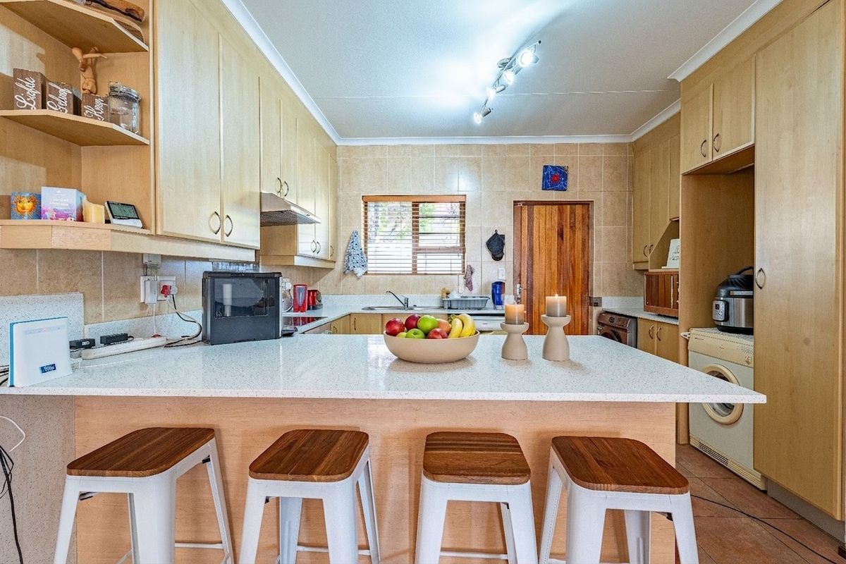 Functional kitchen featuring light wood cabinetry, stone-look countertops, tiled backsplash, and integrated space for laundry appliances.