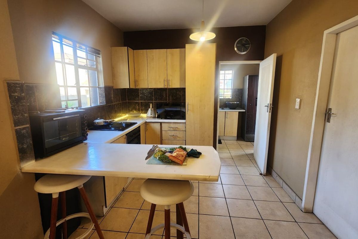 A functional kitchen featuring built-in cabinetry, a breakfast bar, tiled backsplash, and ceramic flooring, with an adjacent scullery area visible.