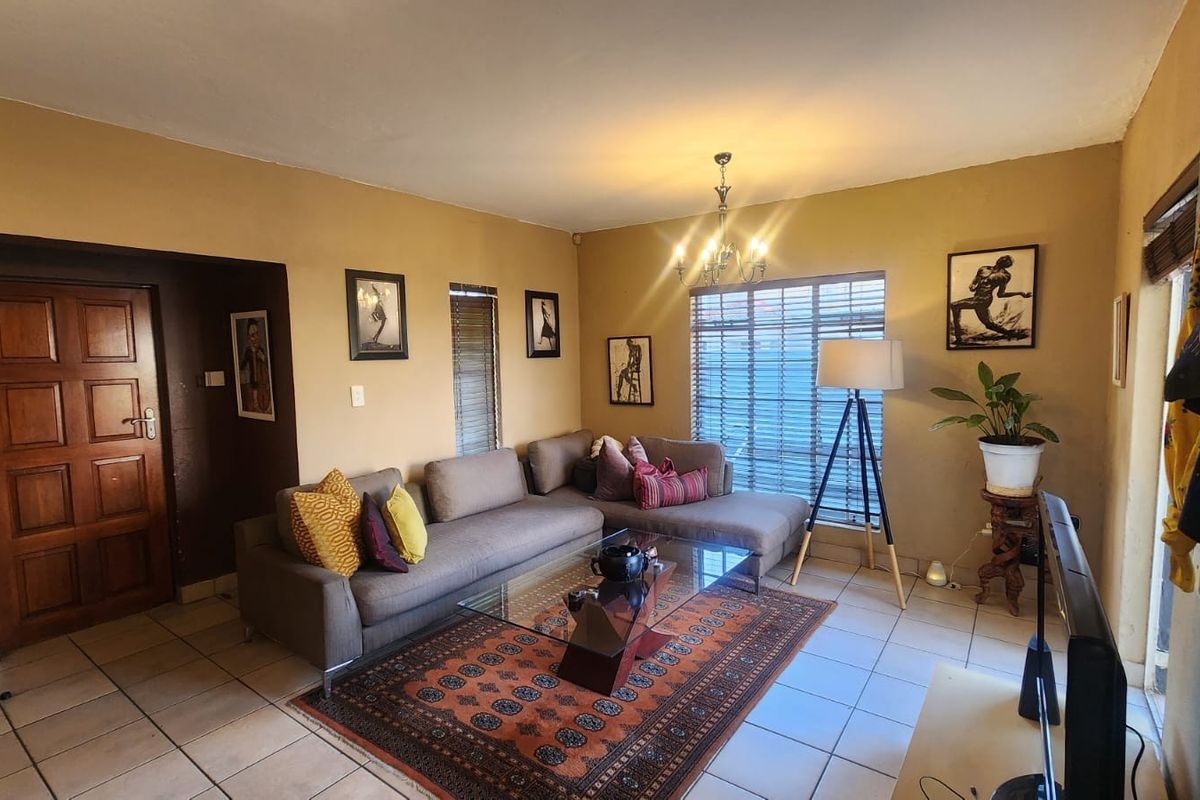 A comfortable living room featuring tiled flooring, a classic chandelier, and natural light through venetian blinds, providing a warm and inviting atmosphere.