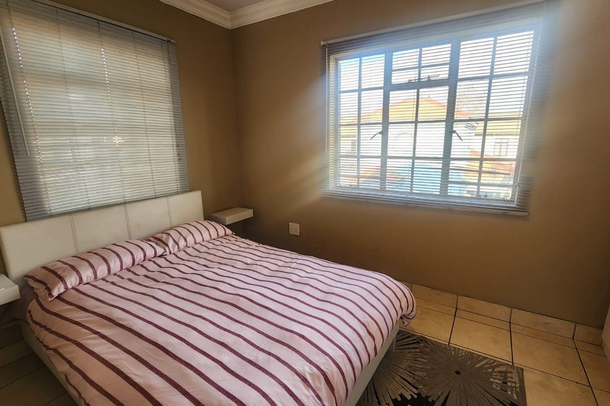 A bedroom featuring tiled flooring, window blinds, and built-in bedside shelves, offering a functional space with natural light.