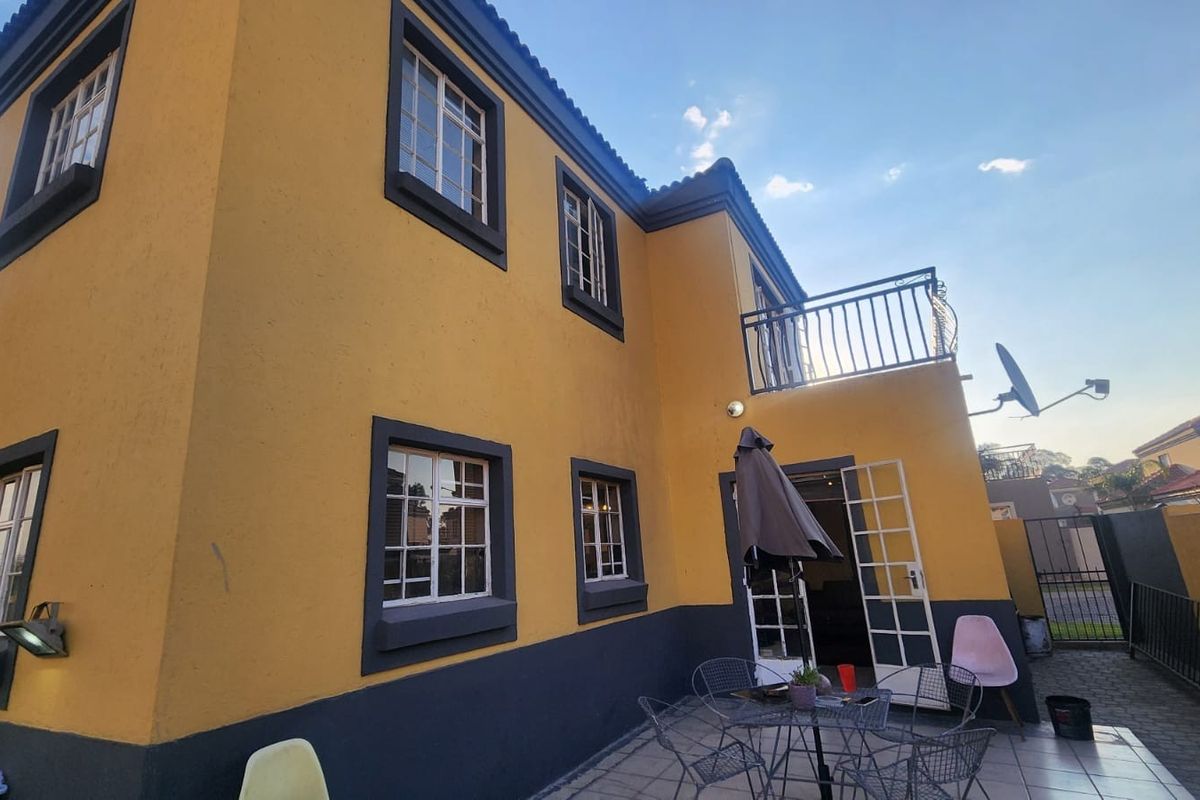 Rear view of a two-story house featuring a tiled patio area, balcony with metal railings, and yellow and grey exterior paint finish.