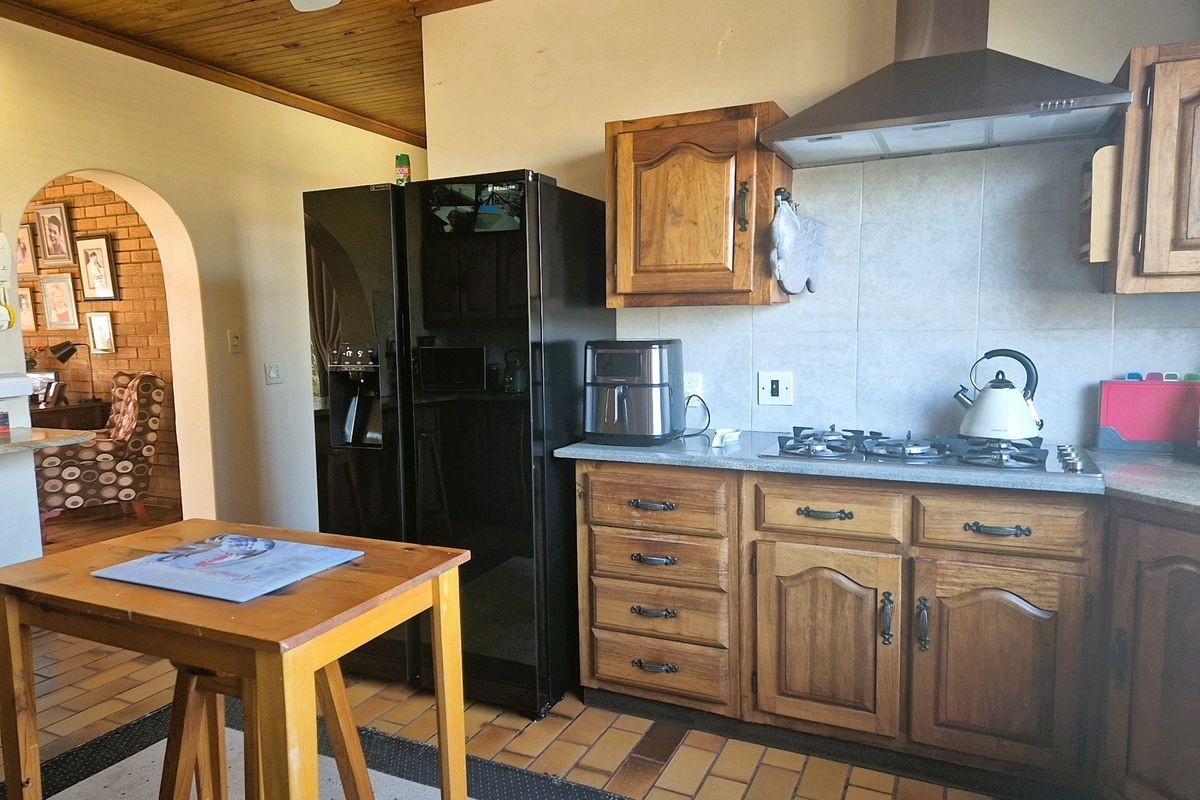 A functional kitchen featuring wooden cabinetry, a gas hob with extractor fan, stone countertops, and traditional terracotta floor tiles.