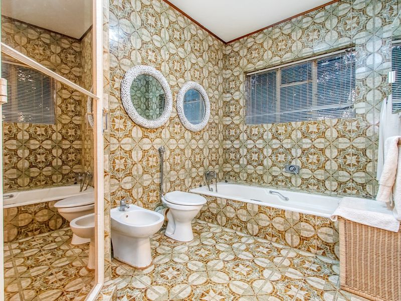 A dated bathroom featuring full-height patterned wall tiles, tiled flooring, a built-in bathtub, a bidet, and a toilet.