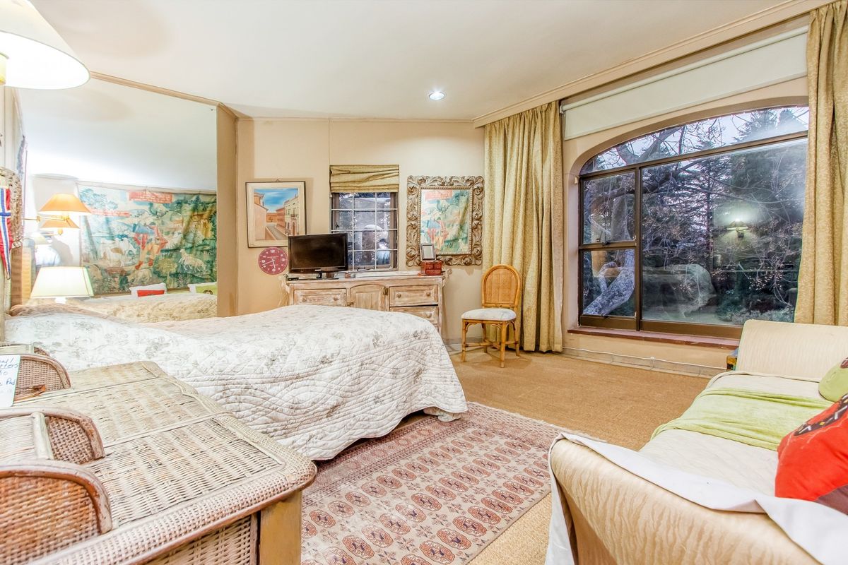 Spacious bedroom featuring a large arched window, carpeted flooring, and a full-length mirrored wall, offering a bright and comfortable living space.