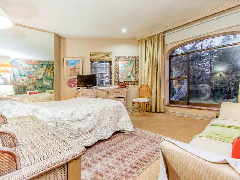 Spacious bedroom featuring a large arched window, carpeted flooring, and a full-length mirrored wall, offering a bright and comfortable living space.