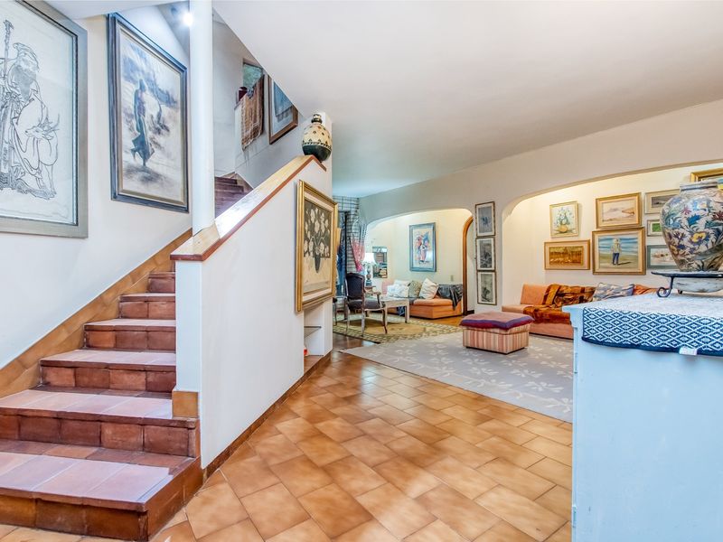 Spacious open-plan living area featuring a tiled staircase with a wooden handrail and classic arched architectural details connecting the living spaces.