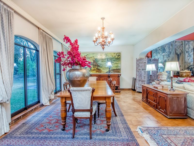 Spacious open-plan living and dining area featuring ceramic tile flooring, arched sliding glass doors providing garden access, and a decorative ceiling chandelier.