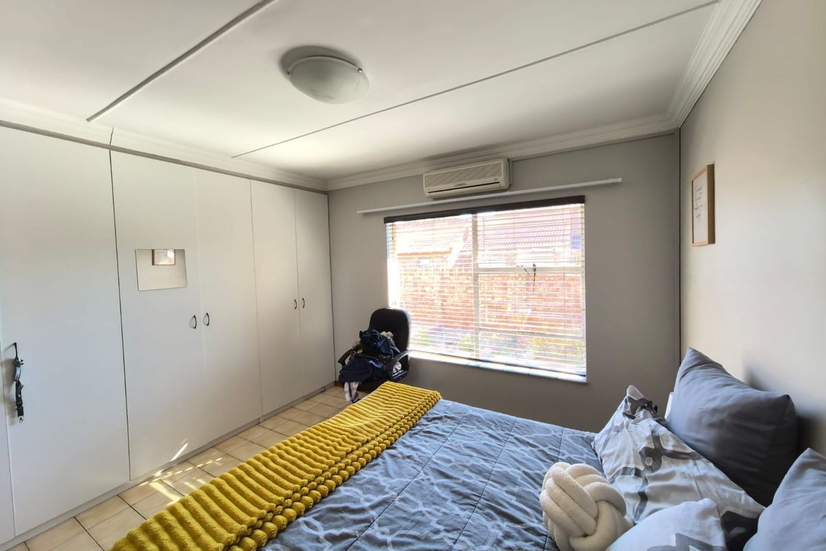 A well-maintained bedroom featuring built-in cupboards, tiled flooring, and a split-system air conditioning unit for climate control.