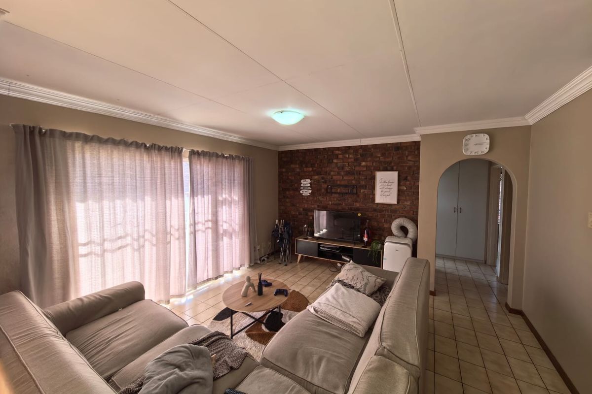 A comfortable living room featuring an exposed brick accent wall, tiled flooring, and an arched entryway leading to the hallway.